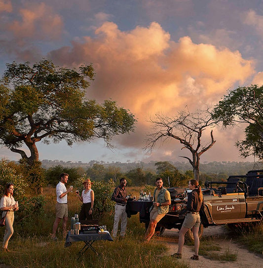Travelers enjoying sunset cocktails while on a safari tour in the wilderness of Southern Africa.