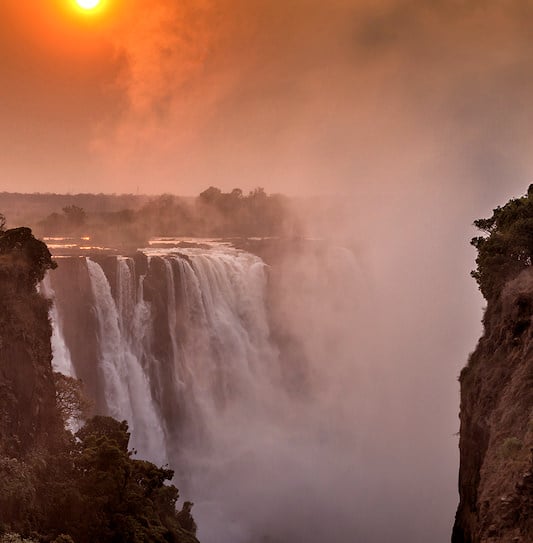 An orange sunset over the deep rocky gorge of Victoria Falls in Zimbabwe.