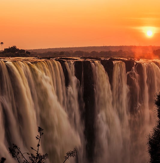A sweeping sunset view of the powerful water cascading over Victoria Falls in Zambia.