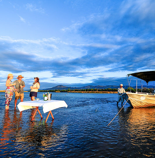 Guests at a safari lodge enjoying sundowners in the shallow waters of the Zambezi River, Zambia.
