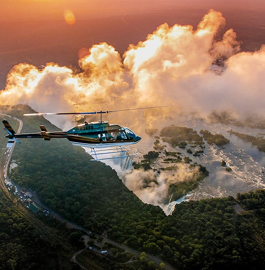A stunning aerial view of a helicopter tour flying over Victoria Falls in Zimbabwe at sunset.