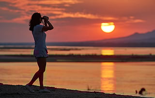 Lady glancing through binoculars at sunset in northern Zimbabwe.